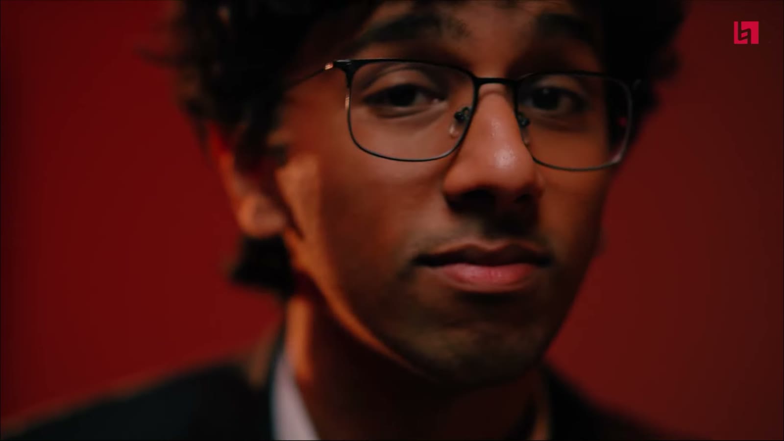 Singer in glasses on a red lit set